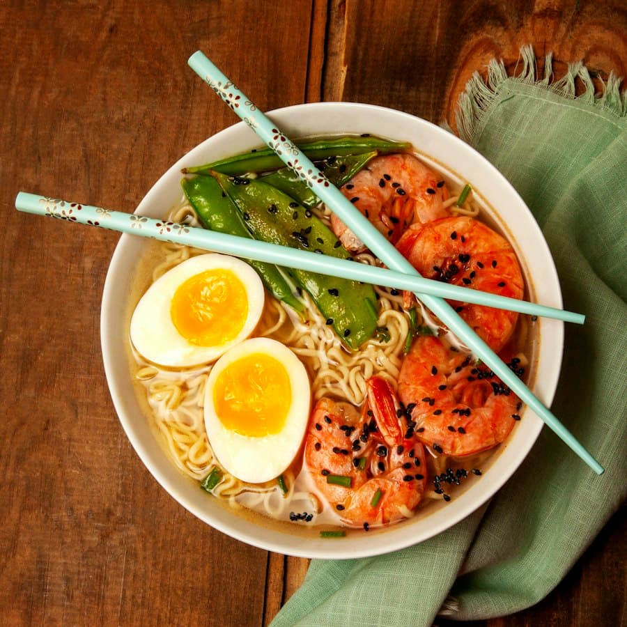 A takeaway bowl of ramen with egg, prawns and greens.